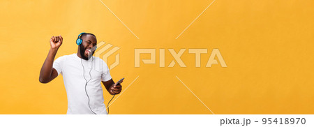African American man with headphones listen and dance with music. Isolated on yellow background African American man with headphones listen and dance with music. Isolated on yellow background 95418970