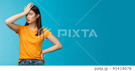 Annoyed arrogant asian girl punch forehead make facepalm sign, roll eyelids irritated pissed, cannot stand lame talks look disappointed ingorant, unwilling to listen, stand blue background 95419076