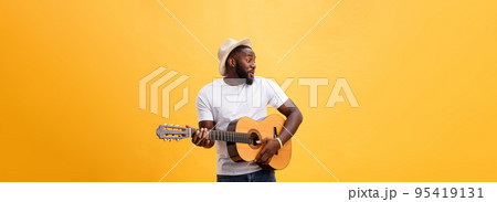 Muscular black man playing guitar, wearing jeans and white tank-top. Isolate over yellow background. Muscular black man playing guitar, wearing jeans and white tank-top. Isolate over yellow background. 95419131