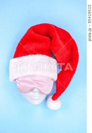 Pink sleeping eye mask on mannequin face with red christmas hat on blue background, sleeping disorder. Holidays, Head accessory. Last minute shopping sickness, Plastic face. 95419515