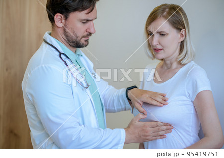 Concentrated mammologist performing the palpation of a woman breast 95419751