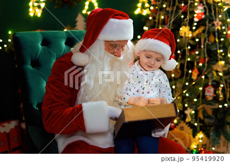 Santa Clause reads Christmas tale to little boy while sitting near Christmas tree. New Year concept 95419920