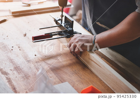 focus hand holding the wood handle, Woodworking operators are using a drill to drill holes in wood to assemble and build wooden tables for customers. focus hand holding the wood handle, Woodworking operators are using a drill to drill holes in wood to assemble and build wooden tables for customers. 95425330