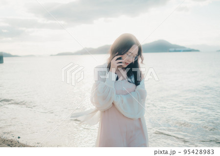 海辺で電話をかける女性の写真 95428983