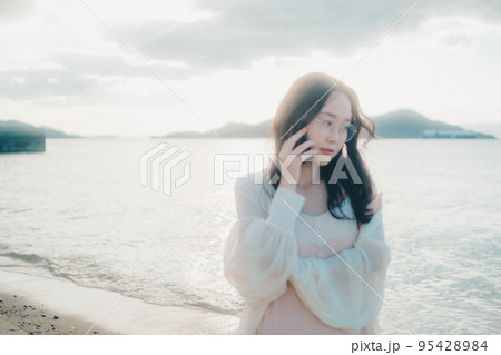 海辺で電話をかける女性の写真 95428984
