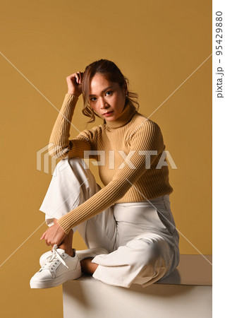 Full length of beautiful woman in warm sweater sitting over brown background. Fashion studio photo 95429880
