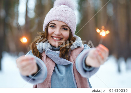 Young girl holding a sparkler in hands. Happy cute girl in knitted hat posing with sparkler. Christmas. 95430056