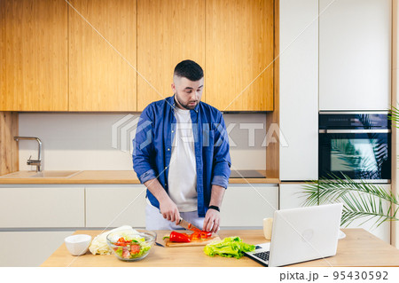 young man cooks at home in the kitchen online, teaches to cook, uses a laptop 95430592