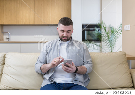 Young man at home sitting on the couch, using the phone, talking on the phone, talking on video 95432013