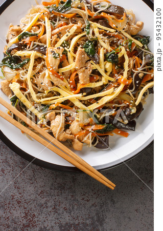 Japchae Korean Glass noodle stir fry with eggs, vegetables and mushrooms closeup on the plate. Vertical top view 95432100