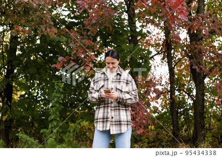 A cute girl stands in the autumn forest with a phone and writes a message 95434338