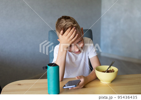 An emotional boy in a white T-shirt connects the speaker to the phone and laughs. 95436435