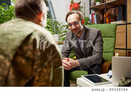 Young distressed woman in military uniform talking to psychologist during therapy session, indoors. Help, support, ptsd, health and harmony concept 95436594