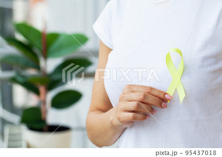Woman in white t-shirt holding and showing yellow awareness ribbon in her hands 95437018