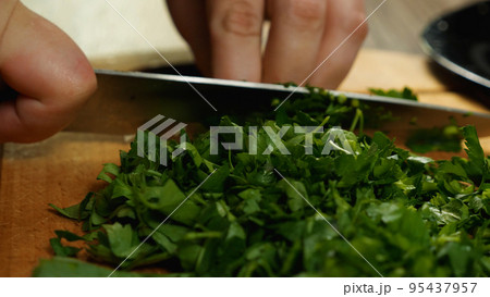 Close-up of a cook slicing parsley with a knife on a cutting board. Side view. Delicious and healthy food. Close-up of a cook slicing parsley with a knife on a cutting board. Side view. Delicious and healthy food. 95437957