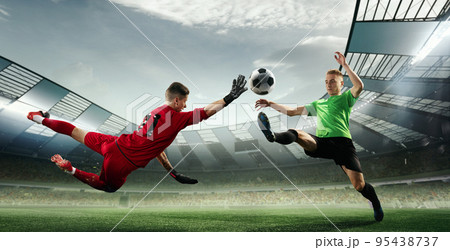 Scoring moment. Football goalkeeper in gates jumping to catching flying ball during soccer match at evening stadium. Sport, action, game, championship 95438737