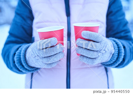 A woman in gloves holds in her hands two red paper cups of hot drink in the winter on the nature, a hot tea in the cold season, a walk and a small trip in the winter. High quality photo 95440550