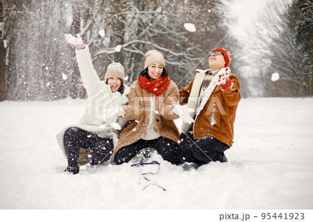 Joyful teens and their beautiful mother spending time together in the winter park. Family throwing a snow. Family wearing warm jackets and knitted hats. Joyful teens and their beautiful mother spending time together in the winter park. Family throwing a snow. Family wearing warm jackets and knitted hats. 95441923