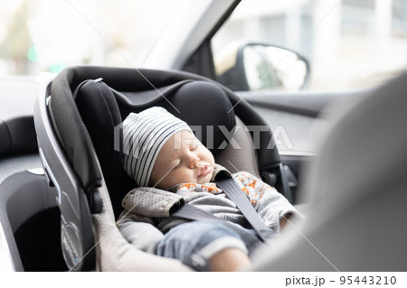 Cute little baby boy sleeping strapped into infant car seat in passenger compartment during car drive. Cute little baby boy sleeping strapped into infant car seat in passenger compartment during car drive. 95443210
