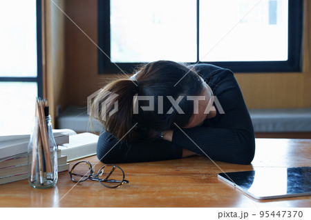 A portrait of a teenage Asian woman sleeping on a desk in the library due to fatigue from studying. A portrait of a teenage Asian woman sleeping on a desk in the library due to fatigue from studying. 95447370