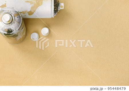 Some used orange aerosol spray cans and nozzles with paint drips lies on a blanket of soft and furry light orange fleece fabric. Classic fashion design color. Graffiti hooliganism concept 95448479