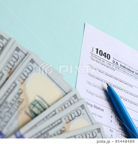 1040 tax form lies near hundred dollar bills and blue pen on a light blue background. US Individual income tax return 1040 tax form lies near hundred dollar bills and blue pen on a light blue background. US Individual income tax return 95448489