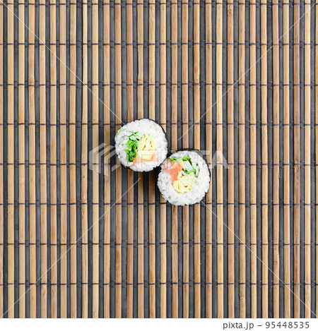 Sushi rolls lies on a bamboo straw serwing mat. Traditional Asian food. Top view. Flat lay minimalism shot with copy space Sushi rolls lies on a bamboo straw serwing mat. Traditional Asian food. Top view. Flat lay minimalism shot with copy space 95448535