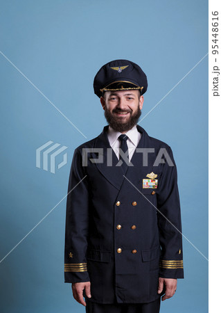 Portrait of airplane captain wearing aviation uniform and hat, plane pilot looking at camera. Aviator with badge on professional jacket, aircrew member on blue background in studio Portrait of airplane captain wearing aviation uniform and hat, plane pilot looking at camera. Aviator with badge on professional jacket, aircrew member on blue background in studio 95448616