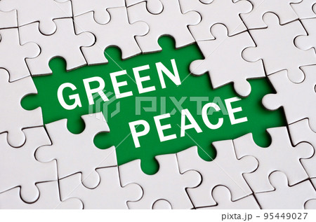 White jigsaw puzzle in assembled state with missing elements forming a green space with white inscription. Green peace 95449027