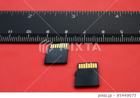 Two small micro SD memory cards lie on a red background next to a black ruler. A small and compact data and information store 95449075