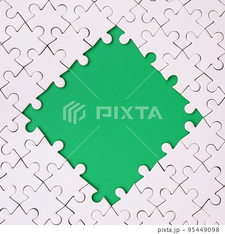 Framing in the form of a rhombus, made of a white jigsaw puzzle around the green space 95449098