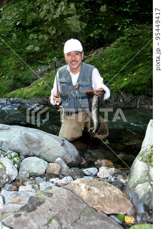 釣れたイワナをランディングネットごと掲げて喜ぶ釣り人 95449417