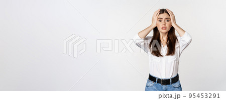 Worried and shocked young woman, looking stunned at disaster, holding hands on head, panicking, standing over white background Worried and shocked young woman, looking stunned at disaster, holding hands on head, panicking, standing over white background 95453291