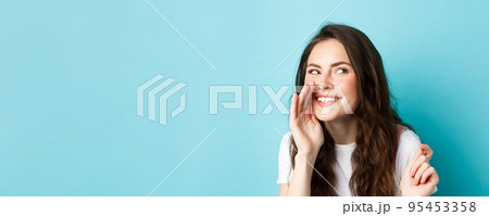 Cunning silly woman spread gossips, talking quiet, telling rumour, smiling and giggle at right side, standing over blue background Cunning silly woman spread gossips, talking quiet, telling rumour, smiling and giggle at right side, standing over blue background 95453358