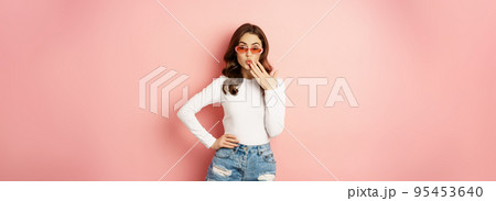 Coquettish and stylish brunette girl, laughing and smiling, wearing sunglasses, wearing white blouse and jeans, pink background Coquettish and stylish brunette girl, laughing and smiling, wearing sunglasses, wearing white blouse and jeans, pink background 95453640