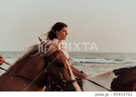 Woman in summer clothes enjoys riding a horse on a beautiful sandy beach at sunset. Selective focus Woman in summer clothes enjoys riding a horse on a beautiful sandy beach at sunset. Selective focus 95453701