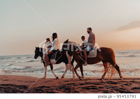 The family spends time with their children while riding horses together on a sandy beach. Selective focus  95453791