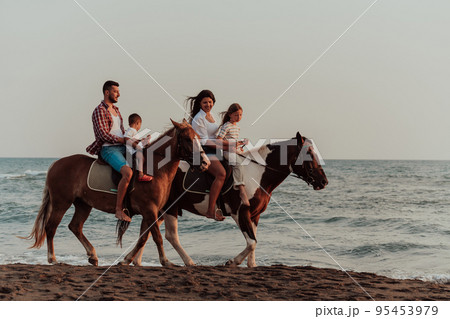 The family spends time with their children while riding horses together on a sandy beach. Selective focus  95453979