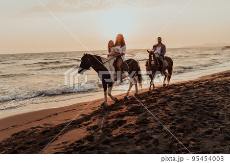 The family spends time with their children while riding horses together on a sandy beach. Selective focus The family spends time with their children while riding horses together on a sandy beach. Selective focus 95454003