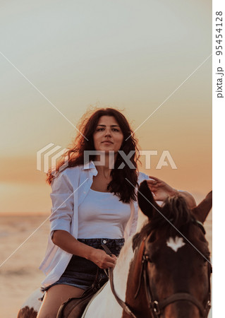 Woman in summer clothes enjoys riding a horse on a beautiful sandy beach at sunset. Selective focus  95454128