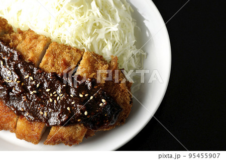 味噌ベースのソースがかかった豚カツとキャベツの千切りを黒背景で俯瞰撮影 95455907