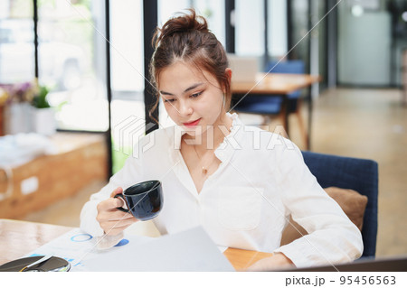 Portrait of a beautiful young woman working on a computer, documenting budget and drinking coffee during a review of the company's investment and earnings financial statements on her desk Portrait of a beautiful young woman working on a computer, documenting budget and drinking coffee during a review of the company's investment and earnings financial statements on her desk 95456563
