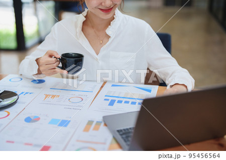 Portrait of a beautiful young woman working on a computer, documenting budget and drinking coffee during a review of the company's investment and earnings financial statements on her desk 95456564