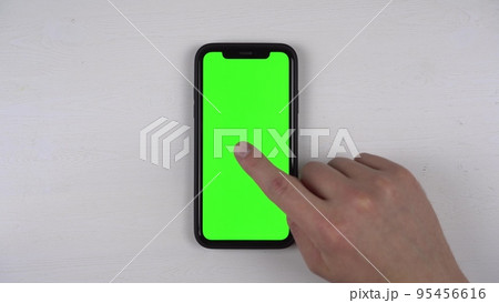 A man uses a phone with a green screen. The man's finger taps on the screen of the smartphone lying on the table. View from above. A man uses a phone with a green screen. The man's finger taps on the screen of the smartphone lying on the table. View from above. 95456616