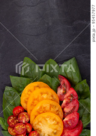 Sliced fresh tomato and basil leaf at black slate background table. Salad ingredients on tabletop 95457977