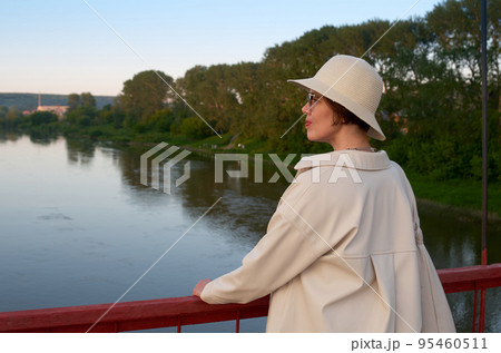 Portrait of travelling woman in hat on bridge against the backdrop of the evening river 95460511