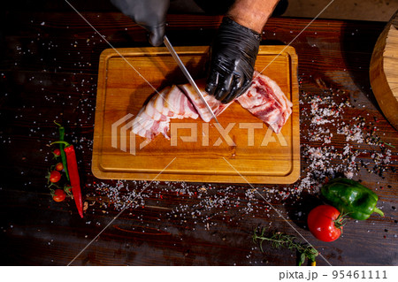 Salted Lard, Raw Pork with Spices on Wooden Cutting Board Studio Photo. A butcher in black gloves thinly slices lard Salted Lard, Raw Pork with Spices on Wooden Cutting Board Studio Photo. A butcher in black gloves thinly slices lard 95461111