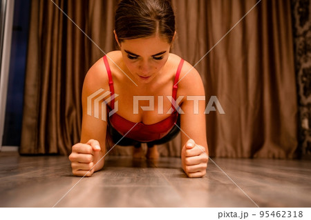 Young woman in red corset and black leather pants. Sexy seductive brunette, fitness instructor doing stretching and pilates on yoga mat at home. Female fitness yoga concept. Role play. Entertainment. 95462318