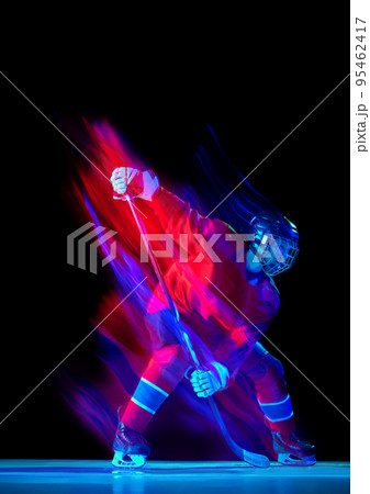 Powerful throw. Male ice hockey player in sports protective uniform in action over dark background in neon mixed light. Achievement, goals Powerful throw. Male ice hockey player in sports protective uniform in action over dark background in neon mixed light. Achievement, goals 95462417