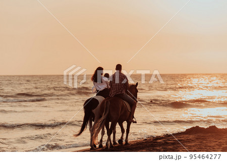 The family spends time with their children while riding horses together on a sandy beach. Selective focus  95464277